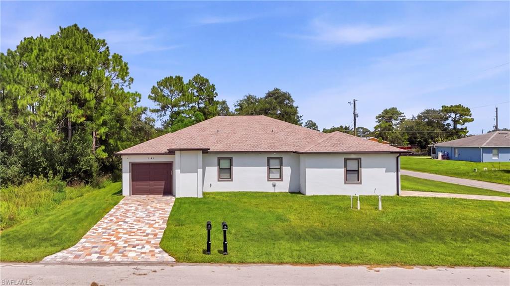 Stucco exterior residence featuring a patterned paver driveway, an attached garage with a wood-look door, and a shingle roof