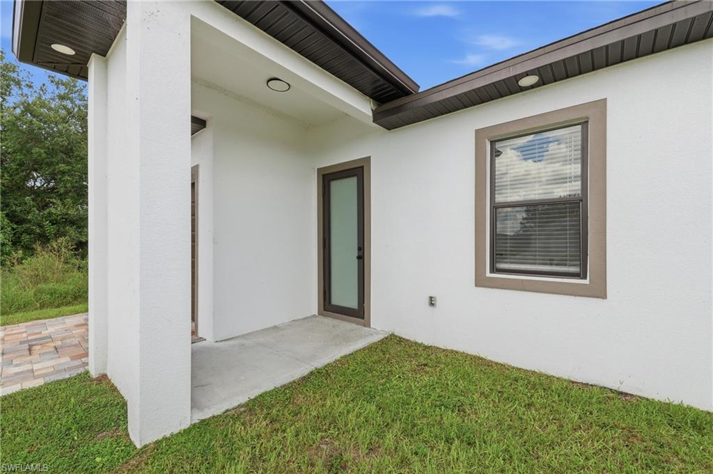 White stucco exterior with a covered entry, dark brown window trim, and a paver pathway