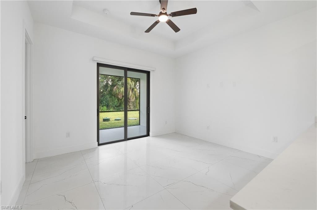 Tray ceiling with integrated lighting, ceiling fan with light fixture, large sliding glass doors, white tile flooring, and a white countertop