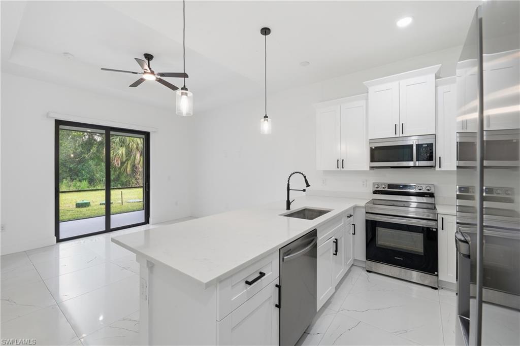 Kitchen featuring white shaker cabinetry, stainless steel appliances, a white island with an integrated sink, and white tile flooring