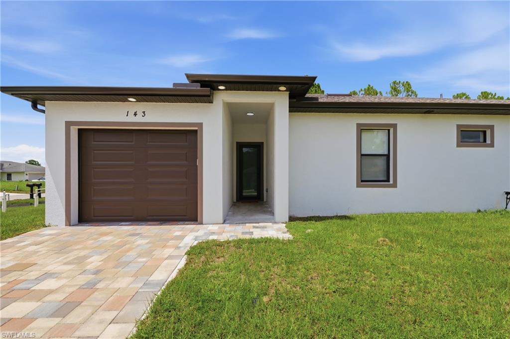 Contemporary stucco exterior with a brown garage door, patterned paver driveway, and an inviting covered entry