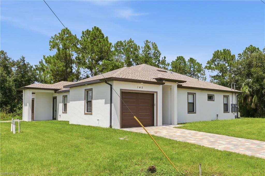 Single-story residence featuring a neutral exterior, paved driveway, attached garage, and surrounding green space