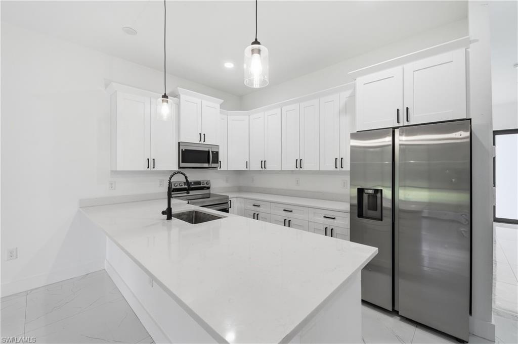 Modern kitchen featuring white cabinetry, stainless steel appliances, a center island, pendant lighting, and light-toned flooring