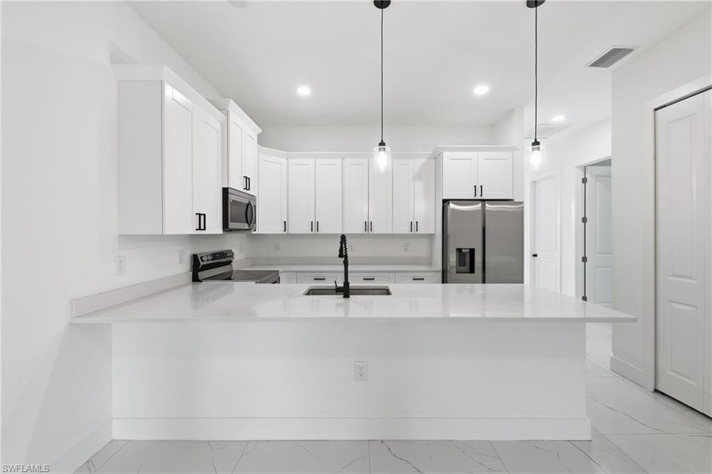 White shaker cabinetry, stainless steel appliances, modern black hardware, light-toned countertops, and pendant lighting
