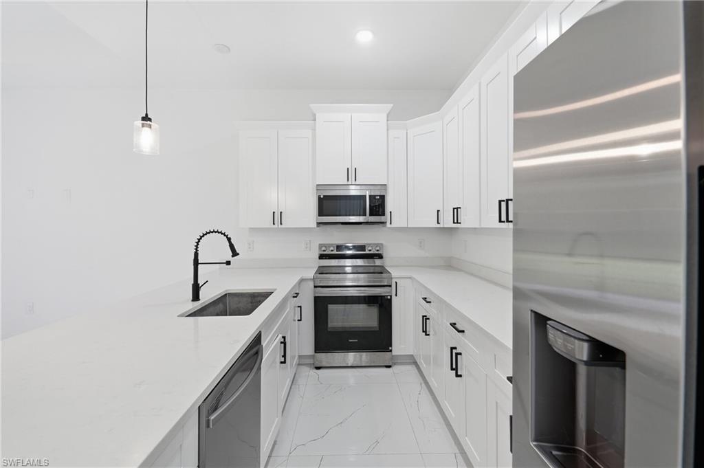 U-shaped kitchen featuring white cabinetry, light-toned countertops, stainless steel appliances, and a matte black faucet