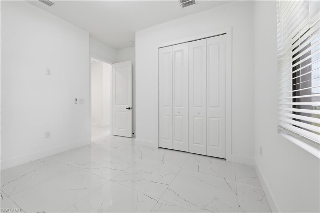 White porcelain tile flooring with subtle veining, white bi-fold closet doors, white interior door with dark hardware, and a window with horizontal blinds