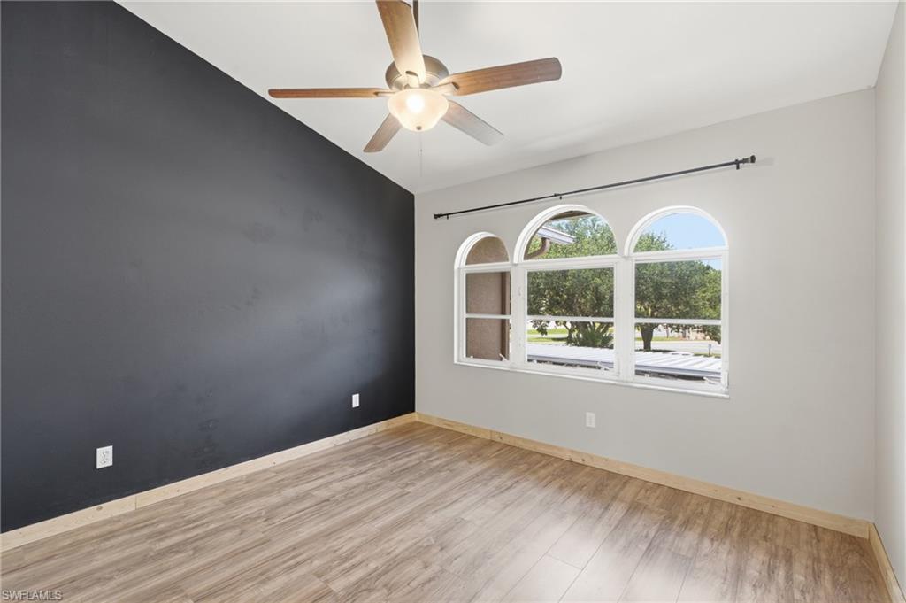 Vaulted ceiling with a ceiling fan, three arched windows, wood-finish flooring, and a contrasting accent wall