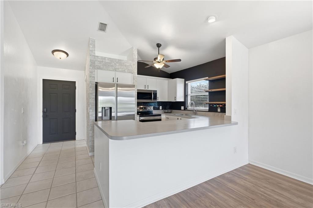 Open-concept kitchen with stainless steel appliances, white cabinetry, integrated sink, and light-toned countertops