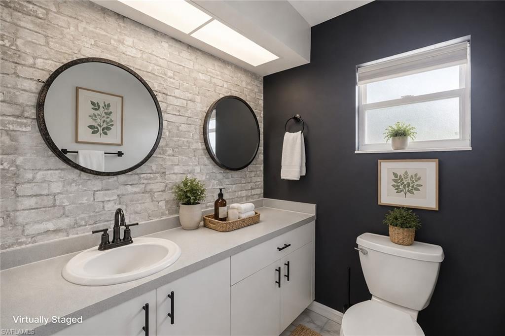 Light-toned brick accent wall, white vanity with integrated sink, dark-toned walls, double round mirrors, and a window with frosted glass