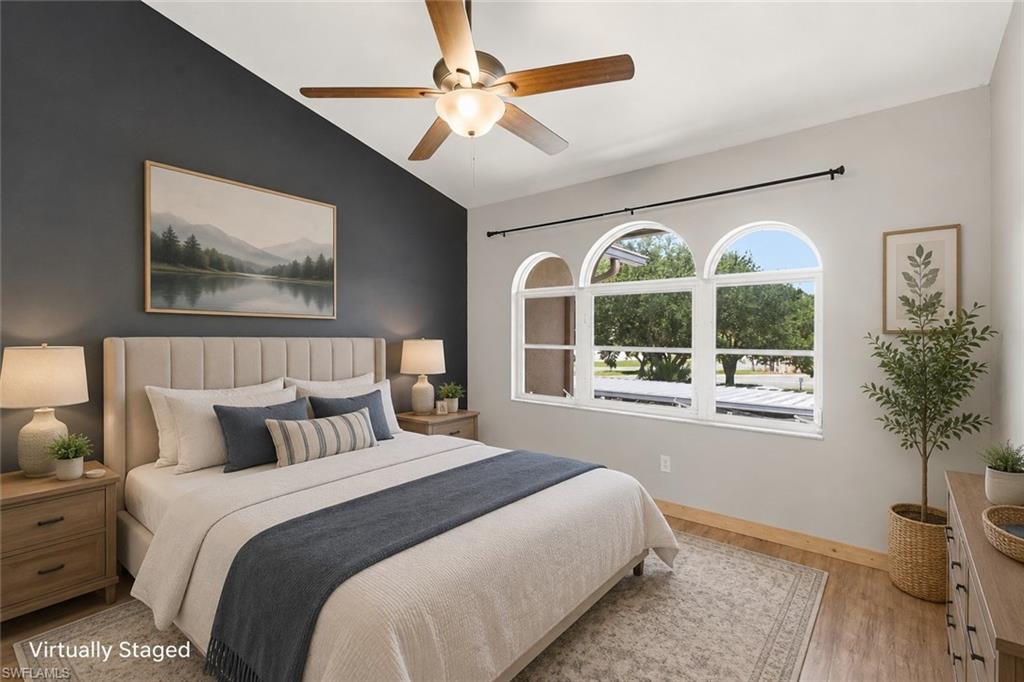 Vaulted ceiling with a ceiling fan, accent wall, wood-finish flooring, and arched windows