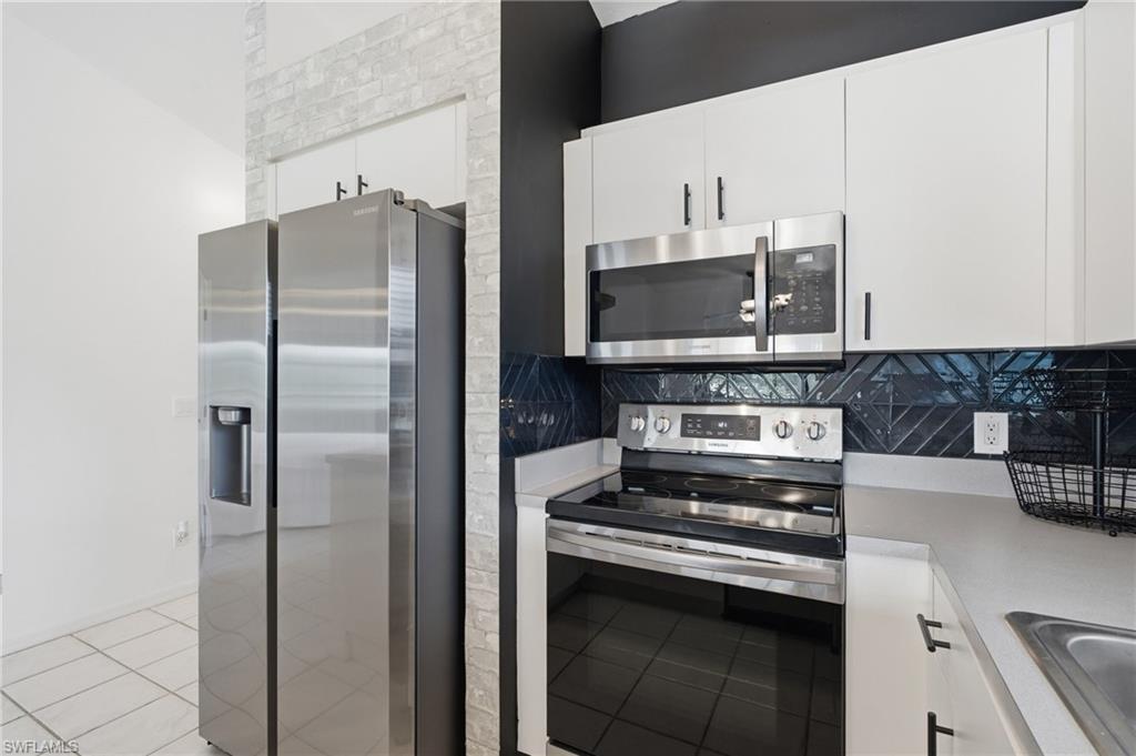 Stainless steel appliances, white cabinetry, dark herringbone tile backsplash, light countertop, and tile flooring
