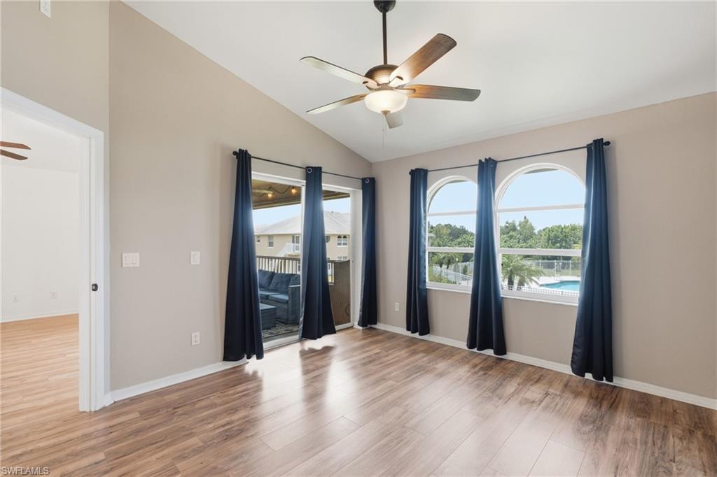 Vaulted ceiling with a ceiling fan, wood-finish flooring, two arched windows, and a sliding glass door to your beautiful lanai area