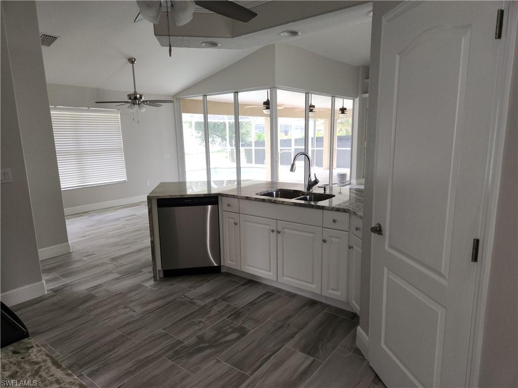 Kitchen with a ceiling fan, stainless steel dishwasher, lofted ceiling, light stone counters, and white cabinets