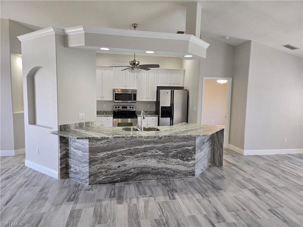 Kitchen featuring stainless steel appliances, white cabinets, light stone countertops, a ceiling fan, and vaulted ceiling