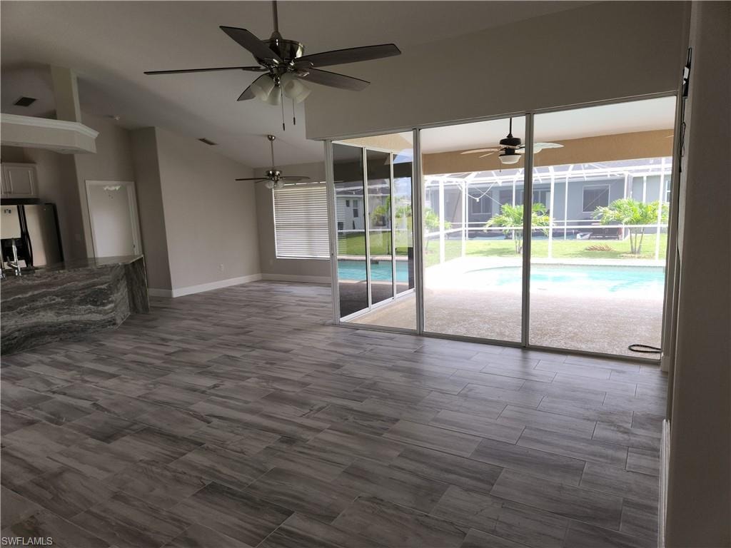 Empty room with lofted ceiling, a ceiling fan, a sunroom, and dark wood-style flooring