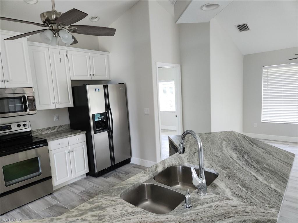 Kitchen with appliances with stainless steel finishes, wood finish floors, ceiling fan, white cabinetry, and light stone countertops
