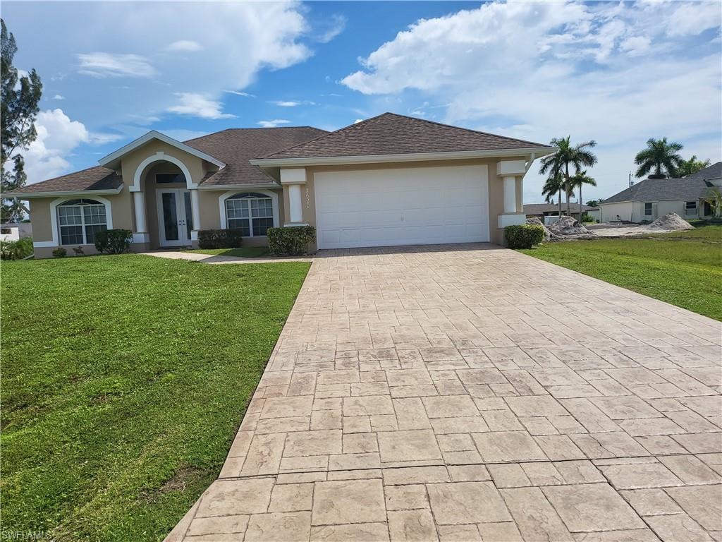 Single story home with stucco siding, decorative driveway, a front lawn, and a garage