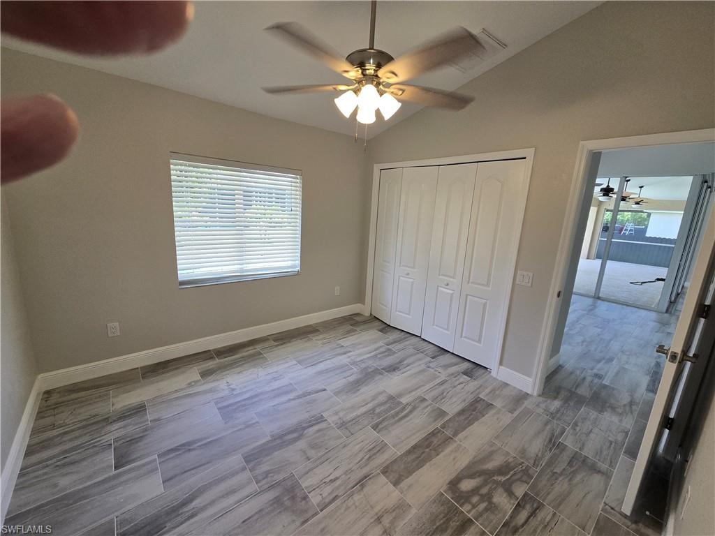 Unfurnished bedroom featuring lofted ceiling, multiple windows, a closet, and a ceiling fan