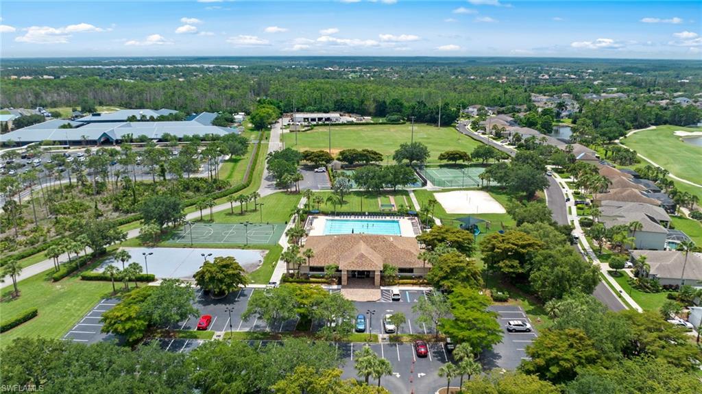 Aerial view showcasing expansive manicured grounds with mature landscaping, resort-style swimming pool, multiple recreational courts, generous parking areas, and lush green spaces surrounding the main clubhouse structure