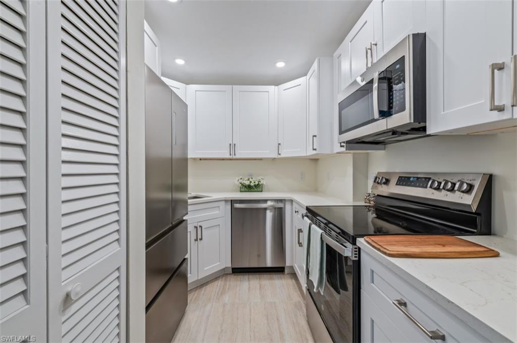 Modern galley kitchen featuring white cabinetry with stainless steel hardware, stainless steel appliances including a double wall oven and microwave, quartz countertops, wood-finish flooring, and recessed ceiling lighting throughout