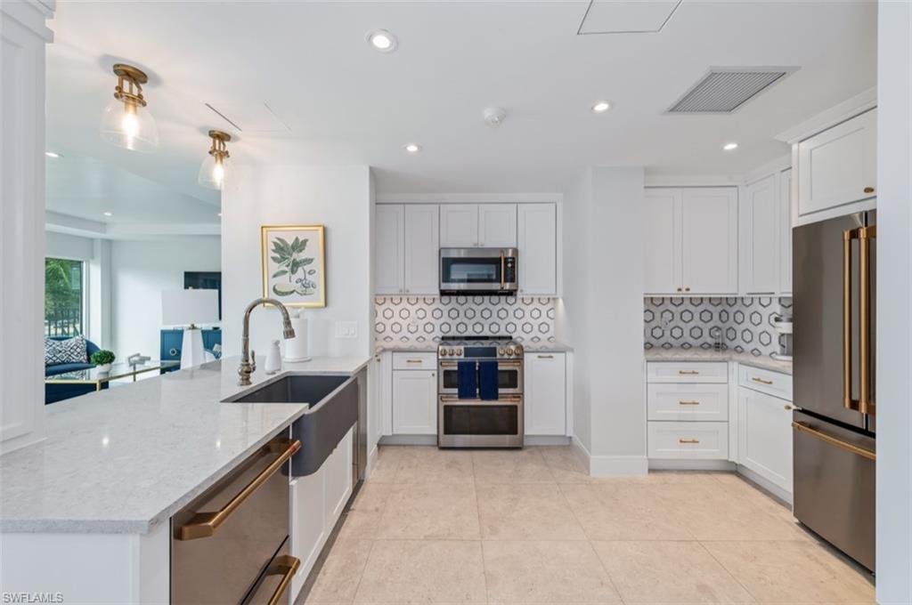 Modern kitchen featuring stainless steel appliances, white cabinetry, a farmhouse sink, and light-toned tile flooring