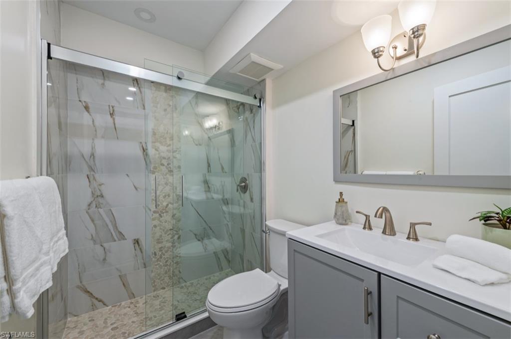 Spa-inspired bathroom featuring a walk-in shower with marble-look tile surround and glass enclosure, dual-sink vanity with gray cabinetry and brushed nickel hardware, large framed mirror, and recessed lighting throughout