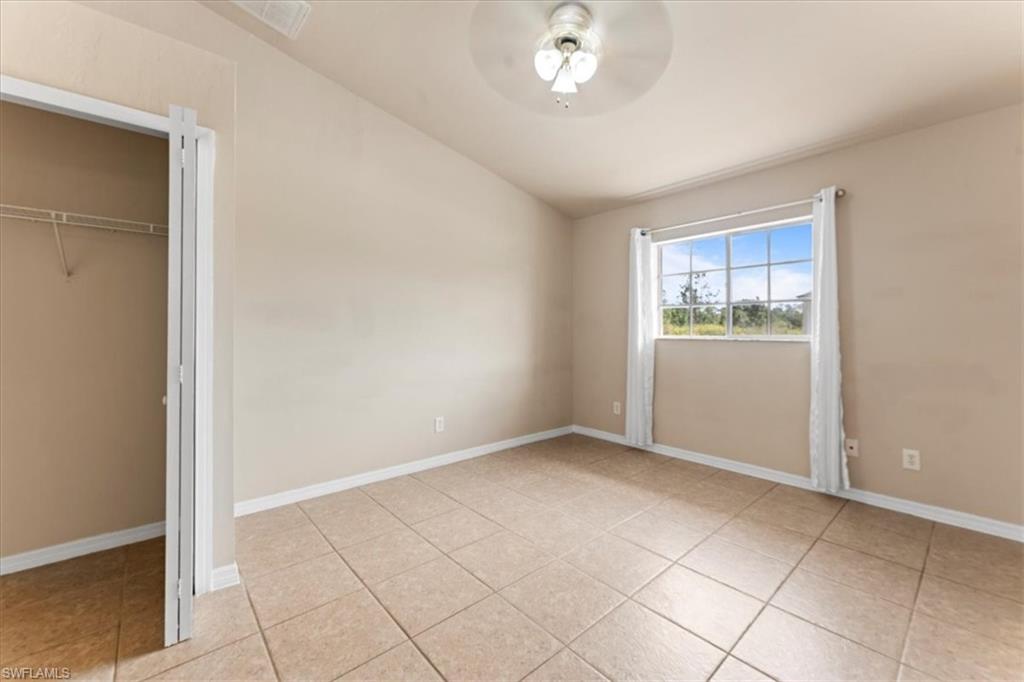 Unfurnished bedroom featuring lofted ceiling, light tile patterned floors, baseboards, and a closet