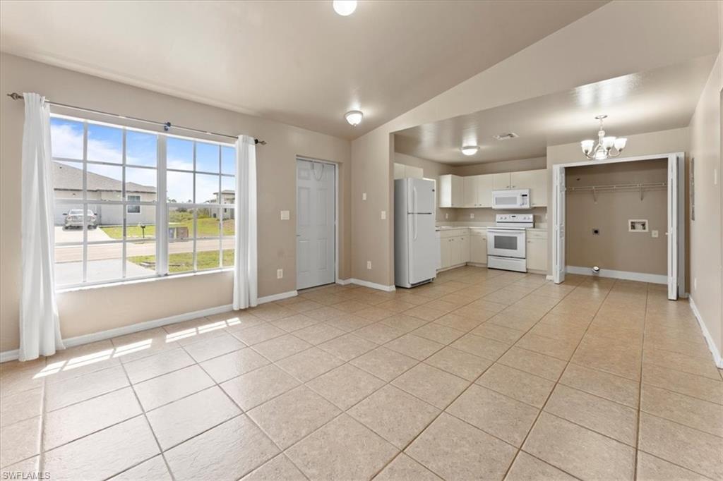 Kitchen featuring white appliances, a chandelier, vaulted ceiling, and light tile patterned flooring