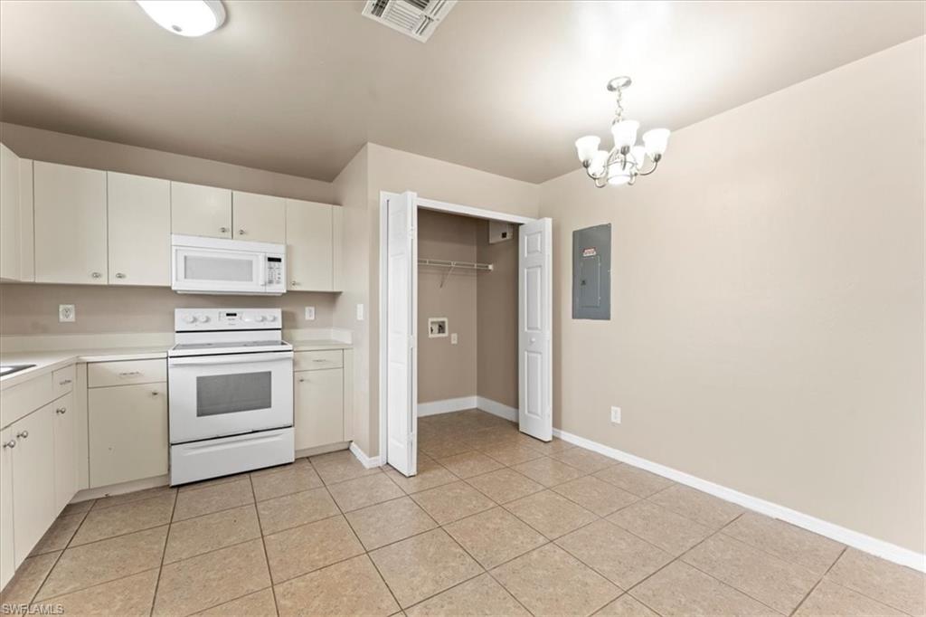 Kitchen with white appliances, electric panel, visible vents, light countertops, and a notable chandelier