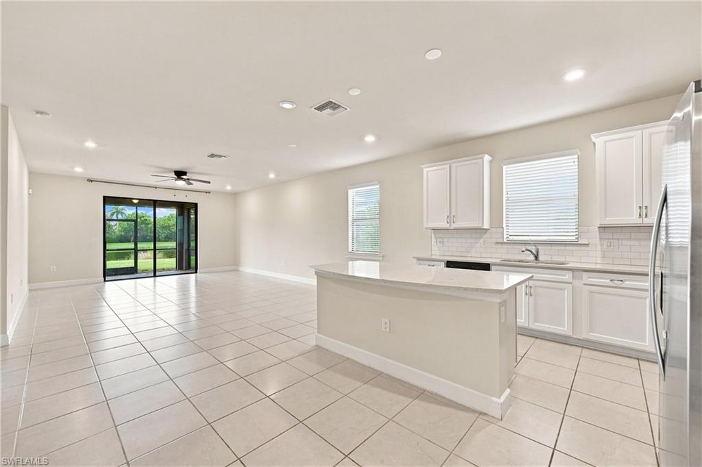 Bright and spacious open-concept kitchen and great room featuring white cabinetry with hardware accents, stainless steel appliances, tile flooring throughout, a large center island with seating, recessed lighting, and French doors opening to the exterior