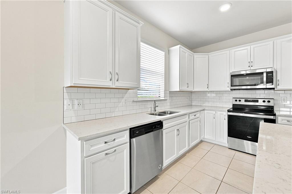 White cabinetry with silver hardware, subway tile backsplash, stainless steel appliances, dual basin sink, and tile flooring