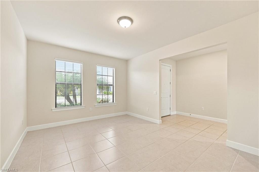 Spacious room featuring tile flooring, two windows with blinds, an overhead flush-mount light fixture, and an open entryway to an additional area