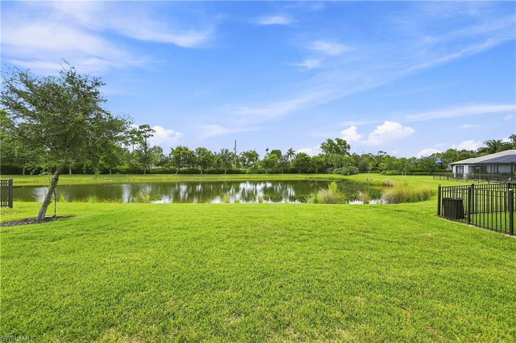 Expansive green lawn with a bordering water feature, mature trees, and perimeter fencing