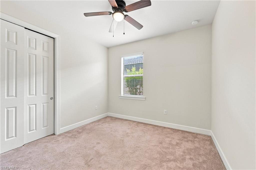 Bright bedroom featuring neutral carpeting, a ceiling fan with integrated lighting, a large window with plantation shutters, a six-panel closet door, and fresh white walls