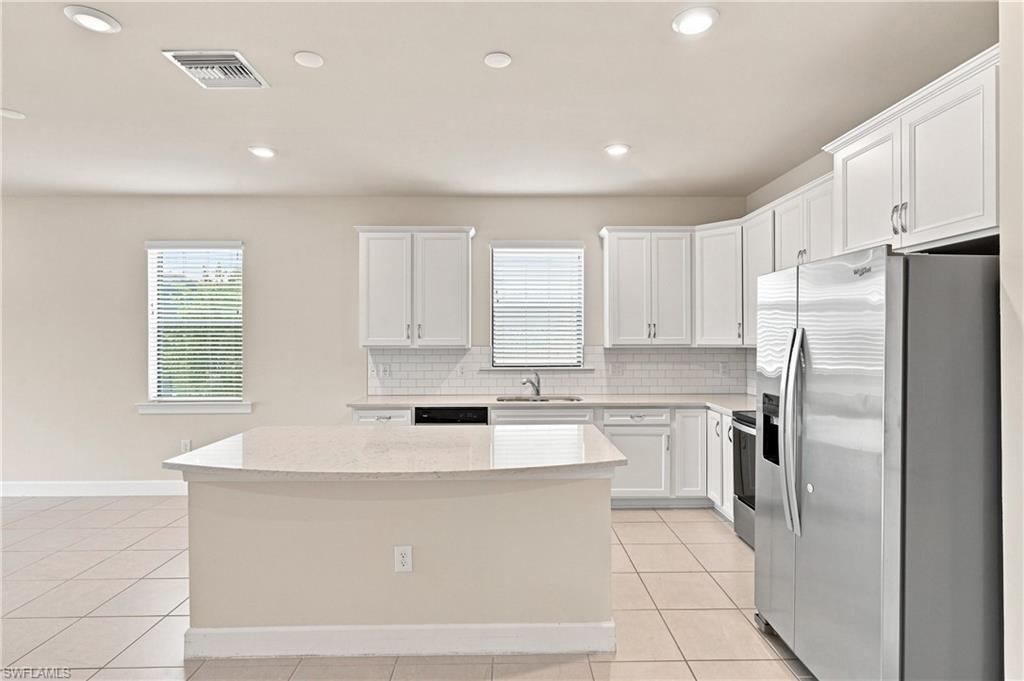 Kitchen featuring a large island with a light-toned countertop, white cabinetry, stainless steel appliances, and a subway tile backsplash