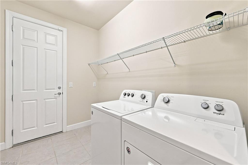 Spacious laundry room featuring side-by-side white appliances with intuitive control panels, tile flooring, wire shelving for storage, and a six-panel entry door providing convenient access from the main living areas