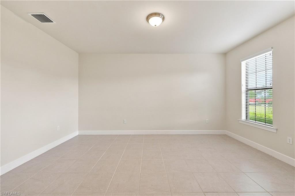 Spacious room featuring neutral wall tones, large window, tile flooring, and a flush-mount ceiling light