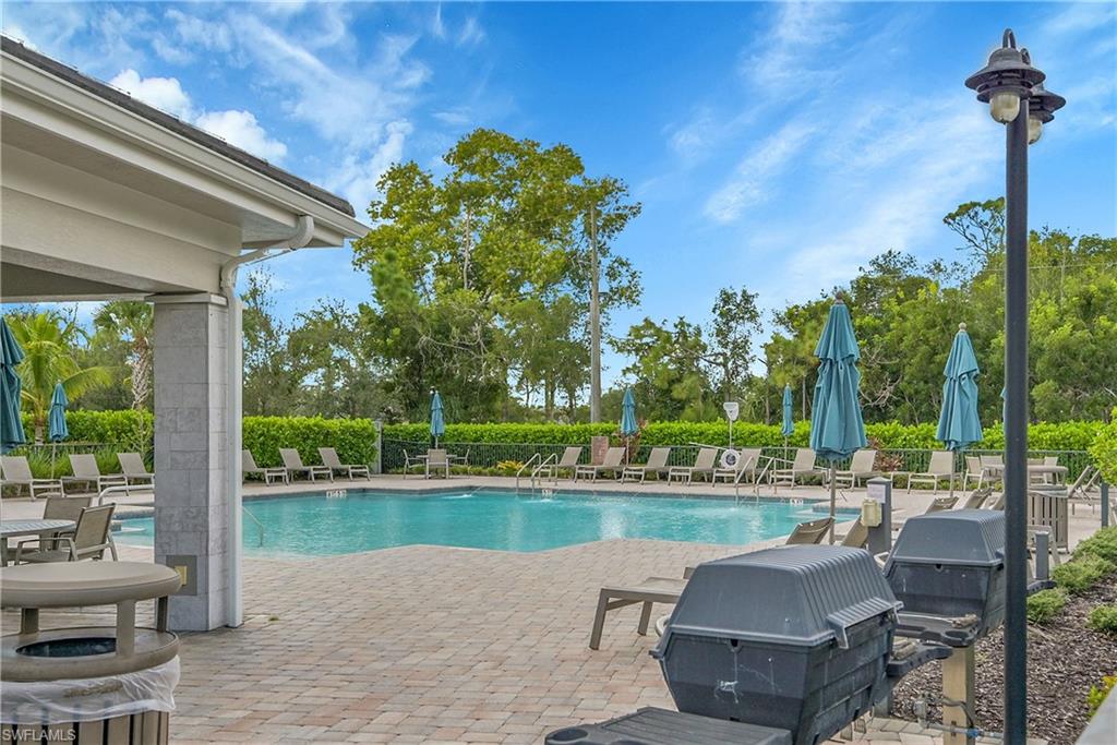 Resort-style pool area featuring crystal-blue waters, expansive paver decking, and mature landscaping with lush greenery