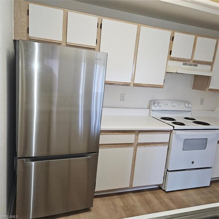 Kitchen featuring light wood-style floors, light countertops, freestanding refrigerator, under cabinet range hood, and white electric stove