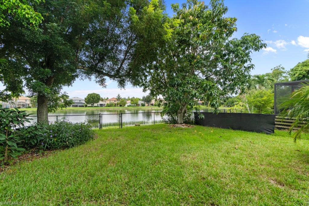 Lush green lawn with mature trees and a black chain link fence bordering a body of water