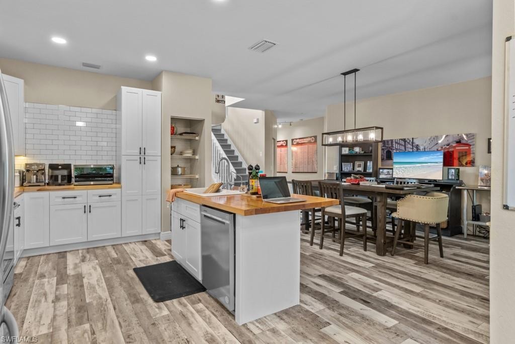 Open-concept kitchen and workspace featuring white cabinetry with brushed nickel hardware, a wood-finish center island with seating, stainless steel appliances, subway tile backsplash, and wood-finish plank flooring throughout