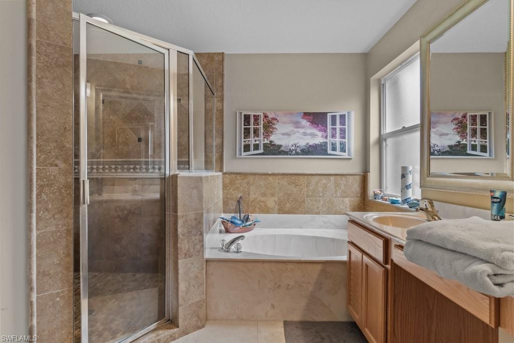 Spa-inspired primary bathroom featuring a frameless glass-enclosed shower with stone tile surround, soaking tub with deck-mounted fixtures, dual vanity with wood cabinetry and stone countertop, large framed mirror, and neutral tile flooring throughout