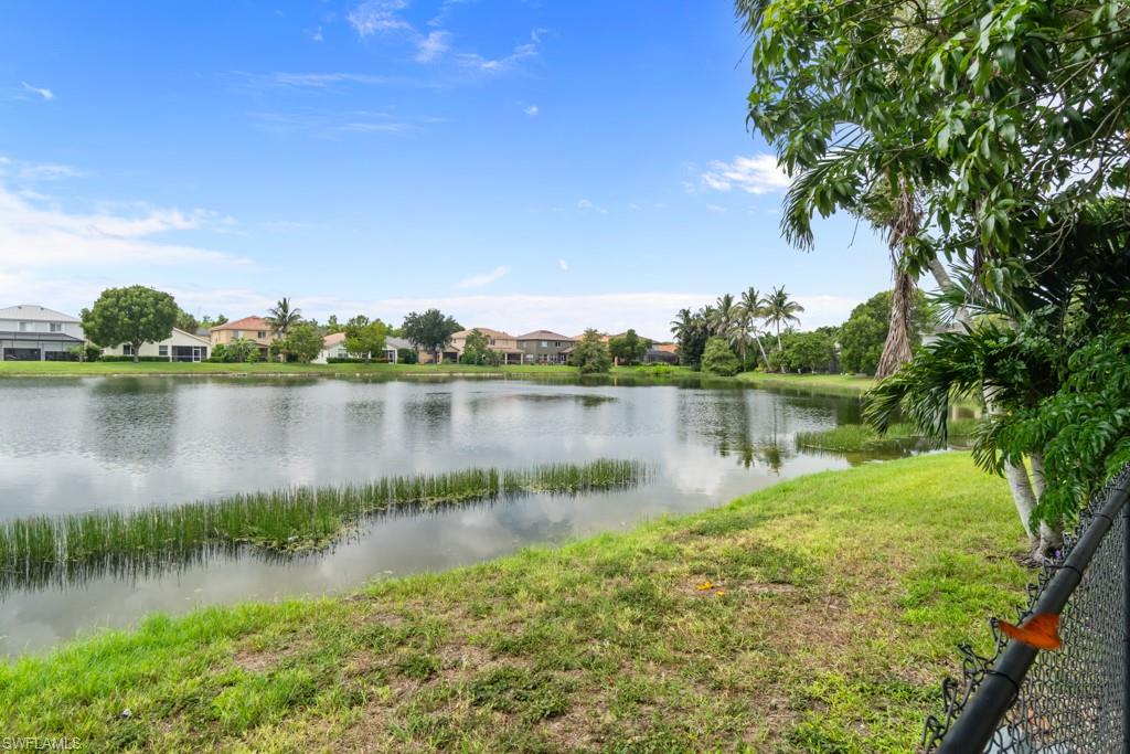 Expansive water feature with natural vegetation and distant residences under a clear sky