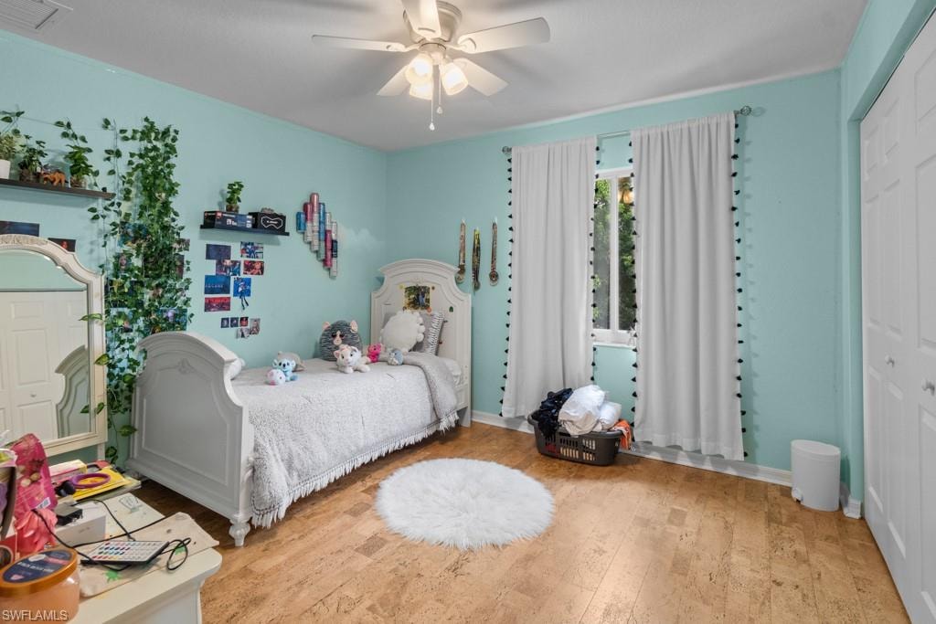 Wood-finish flooring, ceiling fan with integrated lighting, window with trim, and bi-fold closet doors