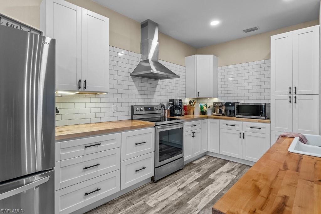 Modern kitchen featuring white shaker-style cabinetry, stainless steel appliances including a gas range and range hood, subway tile backsplash, wood-finish countertops, and wood-look plank flooring throughout
