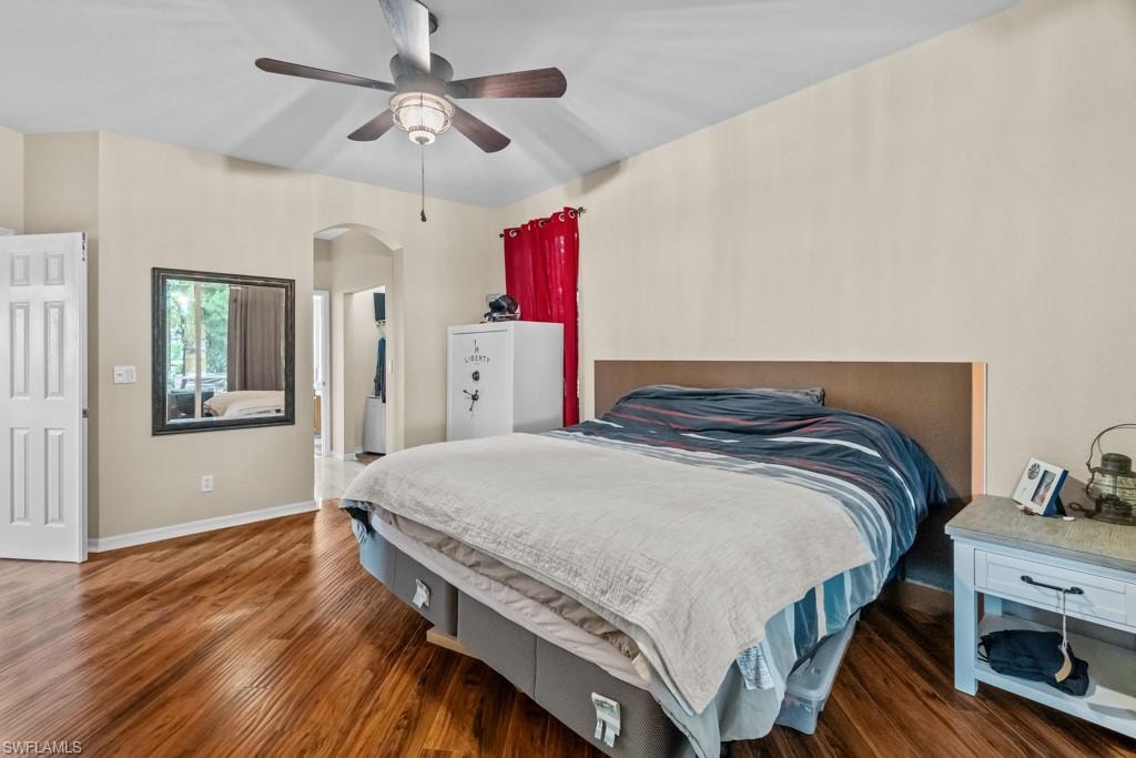 Spacious primary bedroom with warm wood-finish flooring, ceiling fan with integrated lighting, and ample natural light from multiple windows