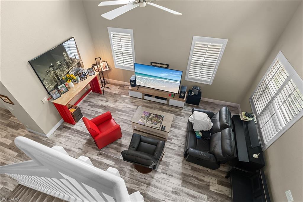 Bright open-concept living space featuring vaulted ceilings with ceiling fan, abundant natural light from multiple skylight windows, wood-finish flooring throughout, and black upholstered seating
