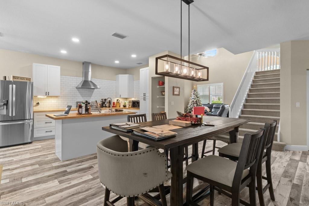 Open-concept living area with wood-finish flooring, a modern kitchen island with wood countertops, white cabinetry, and a full stainless steel appliance package