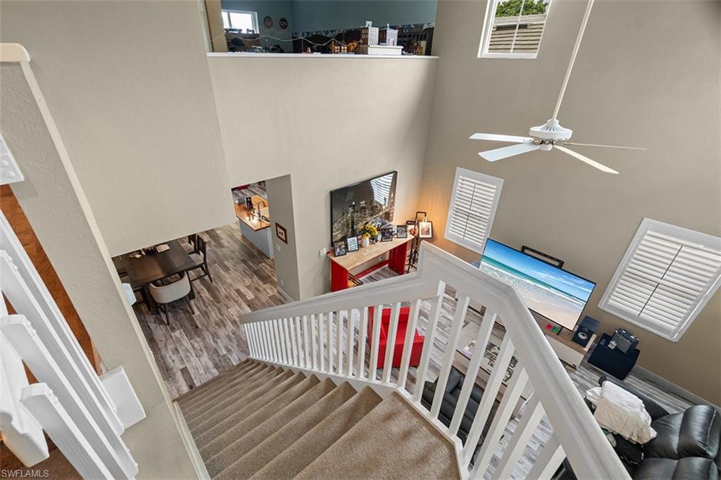 Cathedral ceiling with a white ceiling fan, multiple windows with white plantation shutters, and wood-finish flooring