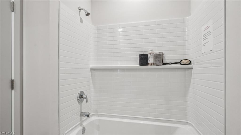 Bathtub and shower combination featuring white subway tile surround, integrated shelf, and chrome fixtures